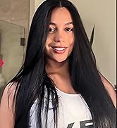 Gros plan d'une personne aux longs cheveux noirs raides et portant un haut blanc. L'image se concentre sur le haut du corps et le visage, montrant une expression souriante.