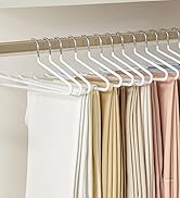 Des cintres en plastique blanc sur une tige métallique contenant divers échantillons de tissu dans les tons de blanc, beige et rose clair