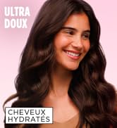 Le texte indique « ULTRA DOUX » et « CHEVEUX HYDRATÉS ». Publicité de produit de beauté sur fond rose montrant de longs cheveux bruns ondulés.