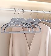 Rangée de cintres identiques en velours gris tenant des vêtements de couleur claire sur une tringle de placard sur un fond neutre