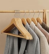 Porte-vêtements en bois avec cintres assortis contenant des vêtements gris. Mélange de cintres en bois et rembourrés visibles sur un mur beige